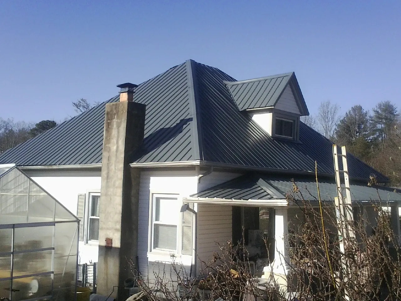 Dark blue standing seam metal roof on a white farmhouse with dormer — Slate & Tile Roof Repair by Roofing Brothers in Nowata