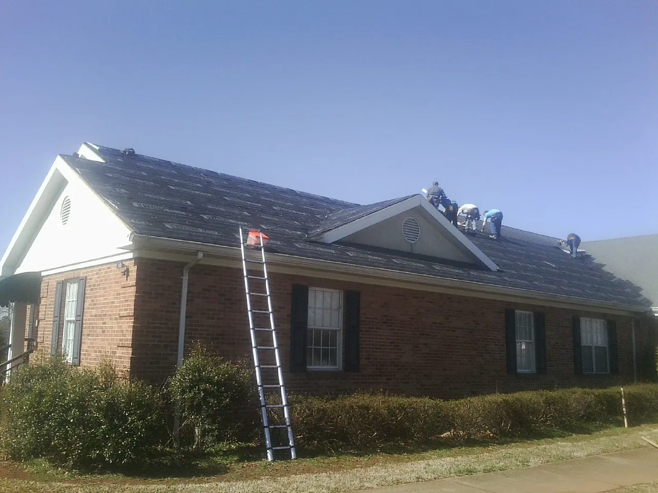 Crew tearing shingles off a brick ranch roof with a ladder set — Emergency Roof Repair work by our crew in Nowata