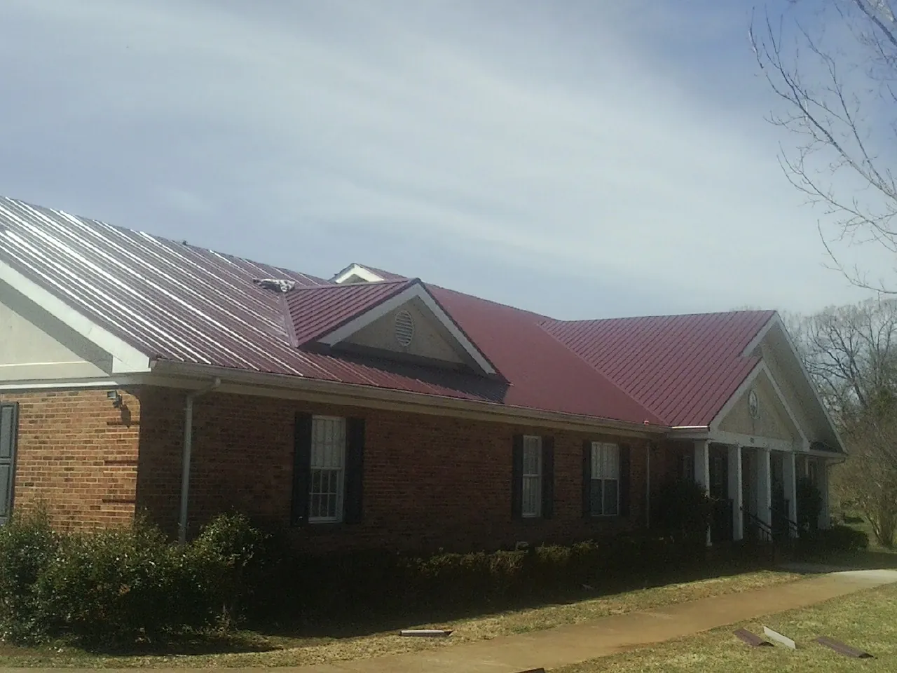 Red metal roof with gabled entries on a long brick building, from a Hail Damage Roof Repair job in Nowata