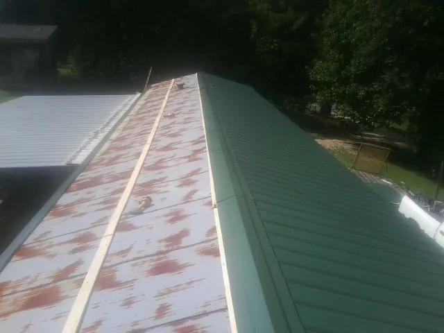 Old rusted panels beside newly installed green metal roofing — Wind Damage Roof Repair by Roofing Brothers in Nowata