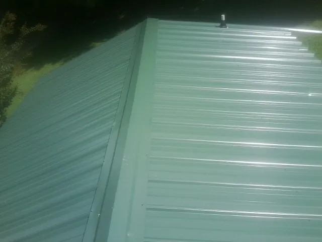 New green metal panels meeting at the ridge of a roof — Flat Roof Repair work by our crew in Nowata