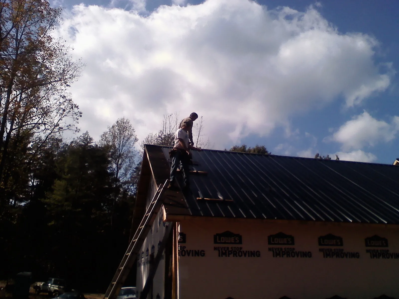 Roofer fastening dark metal panels high against a cloudy sky, from a Roof Inspection job in Nowata