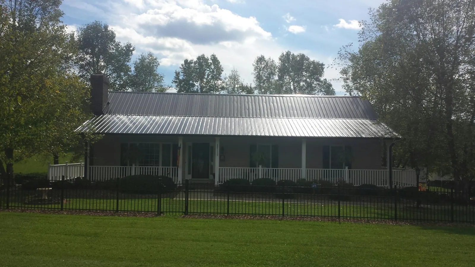 Gray metal roof on a brick ranch with a full width front porch — Gutter Guard Installation work by our crew in Nowata