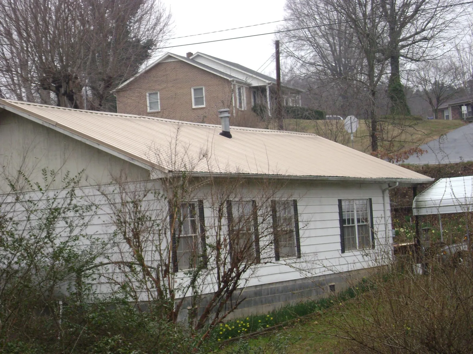 Tan metal roof on a white sided house set into a hillside — Commercial Roofing by Roofing Brothers in Nowata