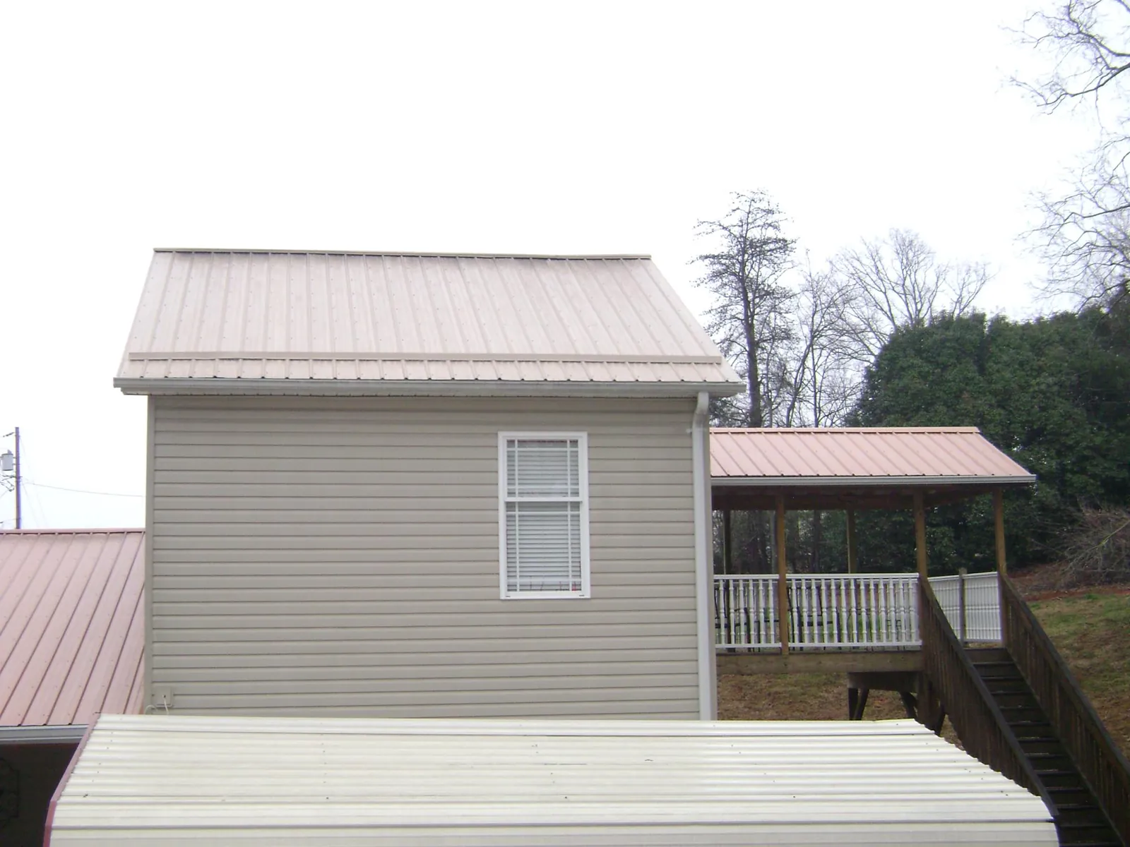 Tan metal roofs on a two story addition and attached porch, from a Roof Replacement job in Nowata